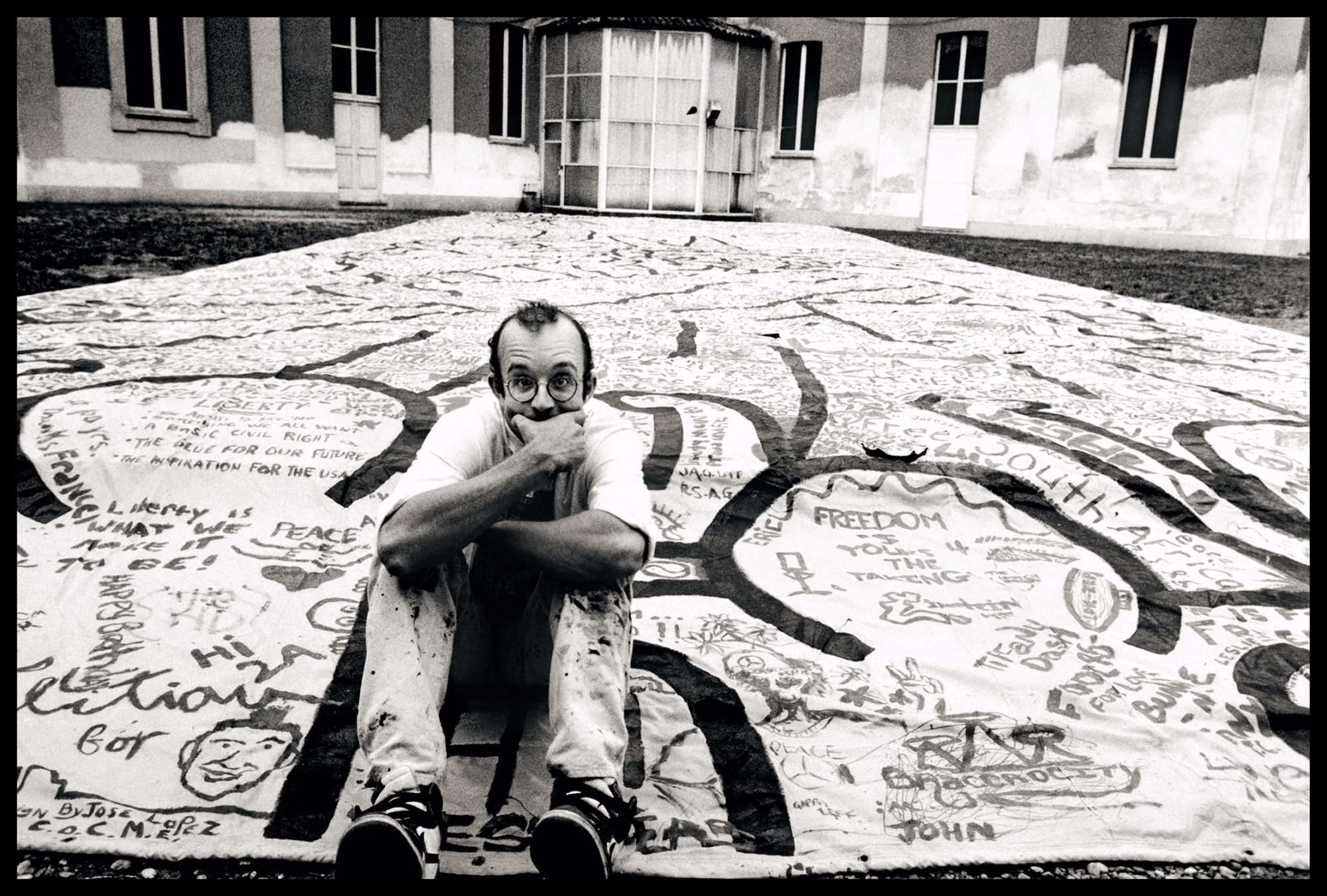 Keith Haring seduto su una sua opera fotografato da Maria Mulas